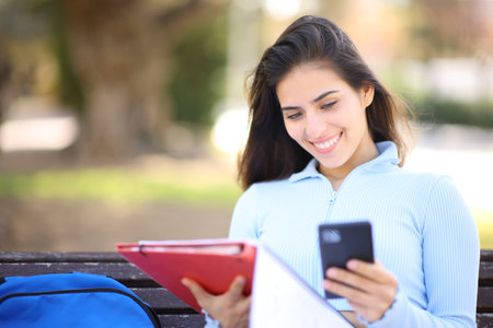 Student studying and using cell phone sitting on a bench in a parkの写真素材