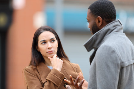 Doubtful woman listening a man talking in the street in winterの写真素材