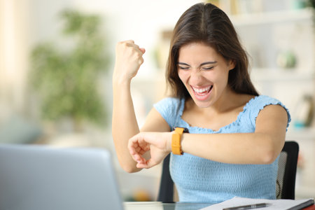 Excited student cheking smartwatch celebrating good news at home