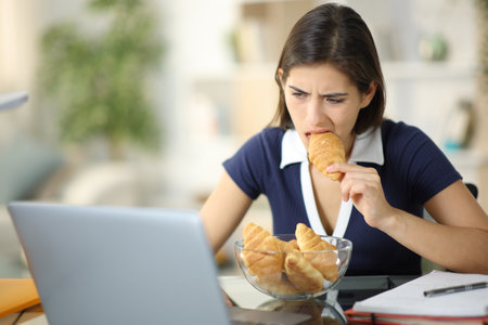 Glutton anxious student eating and studying online at homeの写真素材