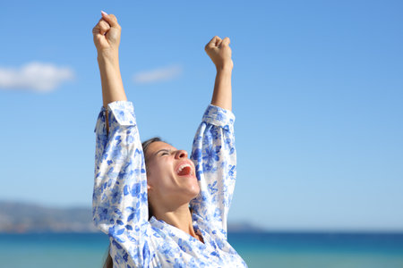Excited woman raising arms on the beach celebrating successの写真素材