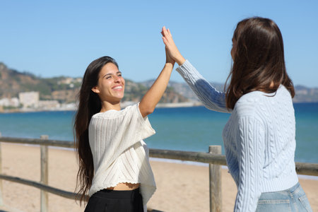Two happy women meeting and giving five on the beachの写真素材