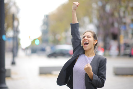 Excited businesswoman celebrating in the street raising arm and screaming