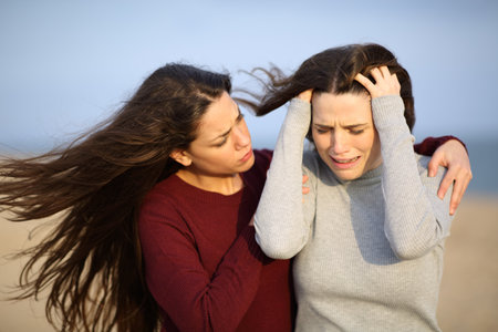 Desperate woman complaining with a friend comforting her on the beachの写真素材