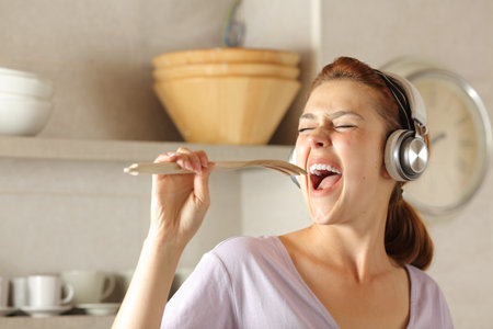 Happy woman in the kitchen wearing headphone  listening music and singingの写真素材