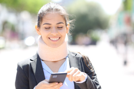 Front view of a happy convalescent executive checking cell phone in the streetの写真素材