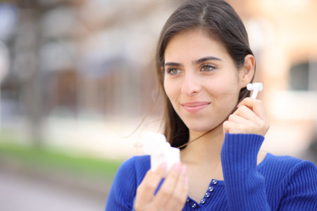 Satisfied woman putting wireless ear bud ready to listen audio in the streetの写真素材