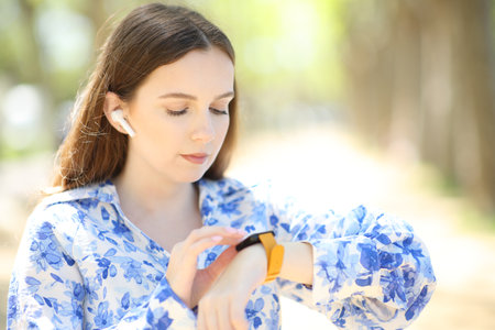 Woman wearing ear buds choosing music in smartwatch in a parkの写真素材