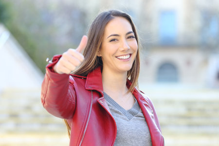 Front view portrait of a happy woman in red gesturing thumb up outside in the streetの写真素材