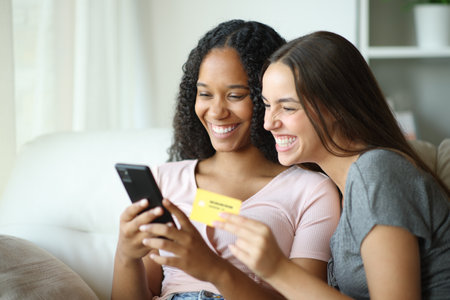 Happy interracial lesbian couple buying online with phone and credit card at homeの写真素材