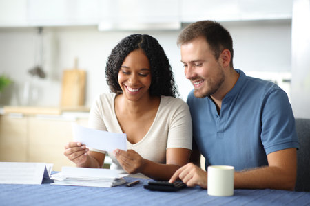 Happy couple reading bank statement in the kitchen at homeの写真素材