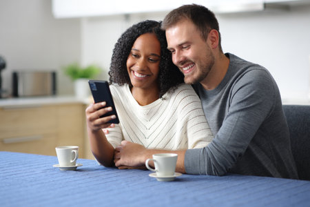 Happy couple checking phone together in the kitchen at homeの写真素材