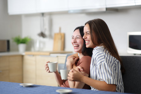 Funny lesbian couple drinking tea or coffee laughing in the kitchen at homeの写真素材