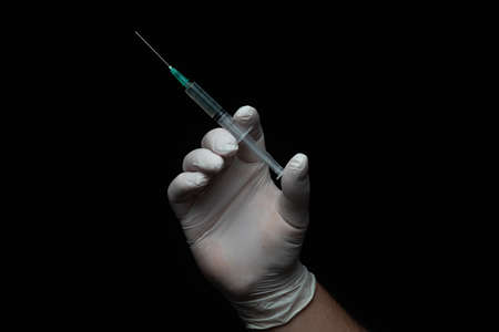 Hand holding the a syringe on black