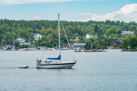 SKURUSUNDET RIVER, SWEDEN - July 11, 2018 : A private sailboat towing a dinghy on Skurusundet riverのeditorial素材