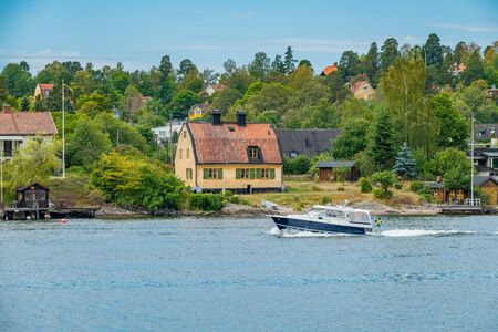 SKURUSUNDET RIVER, SWEDEN - July 11, 2018 : A private motorboat passing by houses on Skurusundet riverのeditorial素材