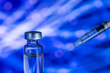 A syringe with the needle point to the vaccine vial on the colorful abstract backgroundの写真素材