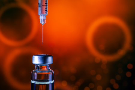 A syringe with the needle point to the vaccine vial on the colorful abstract backgroundの写真素材