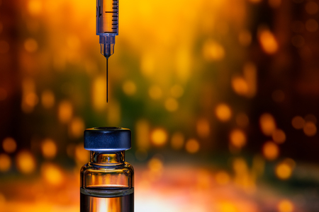 A syringe with the needle point to the vaccine vial on the colorful abstract backgroundの写真素材