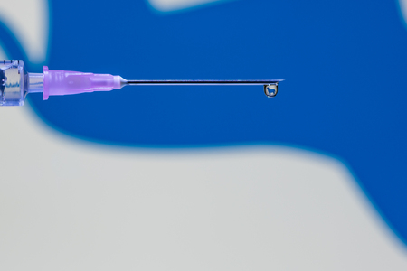 A droplet of vaccine at the tip of the needle and syringe reflecting blue dog symbolの写真素材