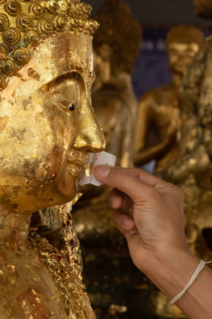 Buddhist believer attaching a gold leaf at the mouth of Buddha statueの写真素材