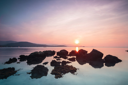 A dramatic scenic landscape shot of the rocks in the ocean with beautiful sky and mountain in background, on a tropical island, shooting in long exposure mode during summer time, Samui Island Thailandの写真素材