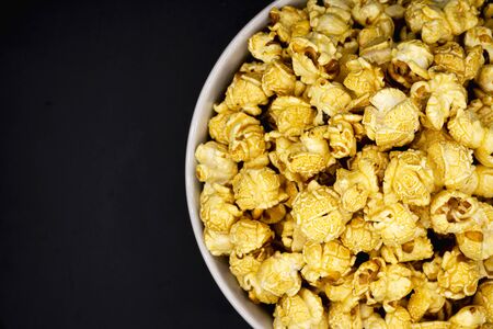 Delicious popcorn with caramel in bowl on black color background