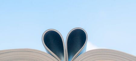 Love of books, reading.  Open book with curled leaves in the shape of a heart and blu sky.の写真素材