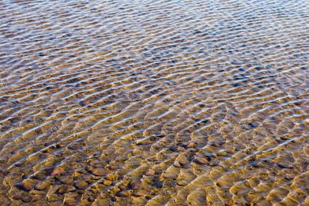 An abstract shot of shallow water on a sand and rock beach.