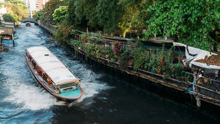 Khlong boat speeds through canal with many green plants along the side.