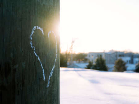 Heart drawn with white chalk on electric pole with sun shining and snow in background.
