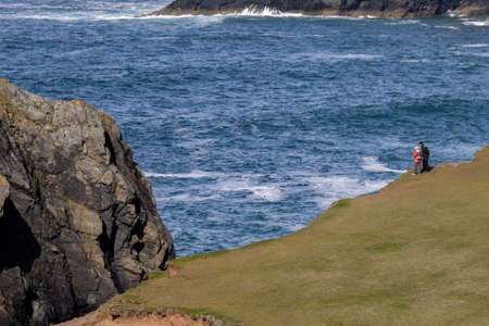 KYNANCE COVE CORNWALL, UK - MAY 14 : People admiring the rugged coastal scenery at Kynance Cove in Cornwall on May 14, 2021. Two unidentified peopleの写真素材