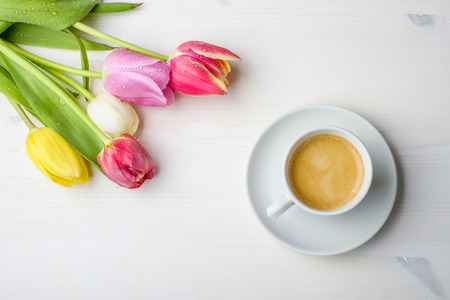 Coffee and tulips on a white wood table with some water on the tulipsの写真素材