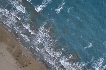 White foamy sea waves splash to deserted sandy beach in the evening. Evening surf. Aerial top view...