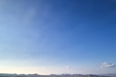 Bright autumn blue sky with white clouds and mountains at the horizon. Background or texture image...