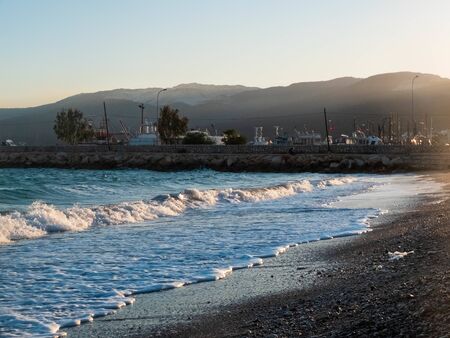 Splashing foamy waves of the sea beat on the pebble beach in the rays of the sunset.の写真素材