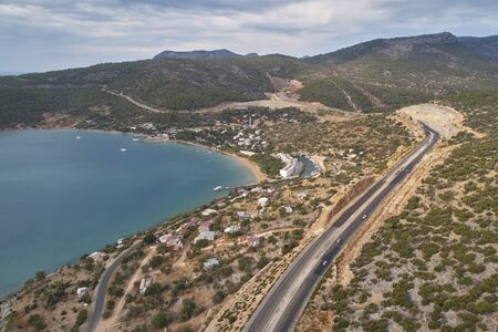 Mountain highway road, nautical vessels in the sea harbor and pine-covered mountain ranges in the morning. Aerial viewの写真素材