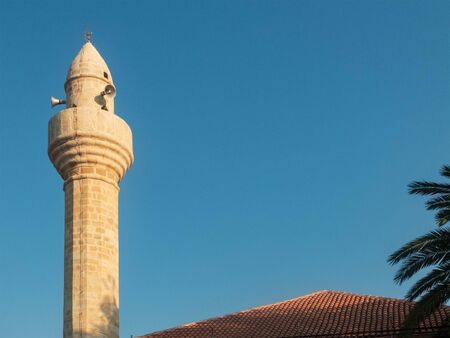 Mosque minaret opposite evening blue sky and palm tree.