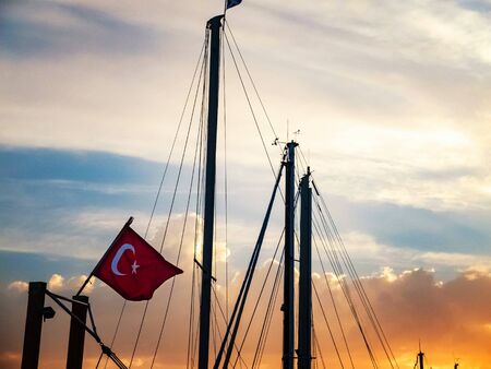 Turkish flag is waving on the top of nautical vessel against masts and sky at the backgroundの写真素材