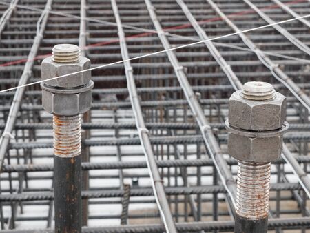 Two steel anchor bolts with screw nuts and steel grid on tower crane footing reinforcement.