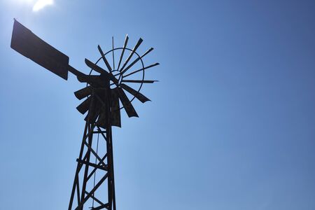 old rusty wind mill or wind pump opposite clear blue sky.