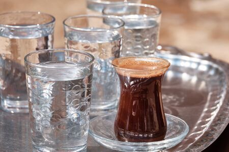 Glasses of water and Turkish coffee are on a metal tray.の写真素材