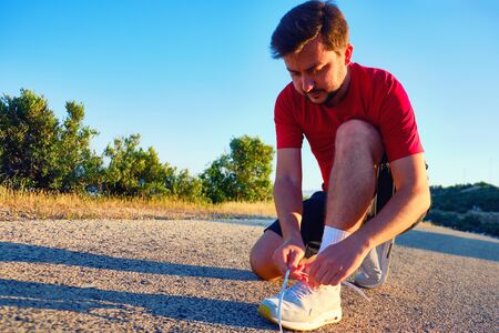 man tying laces during morning jogging in the countryside