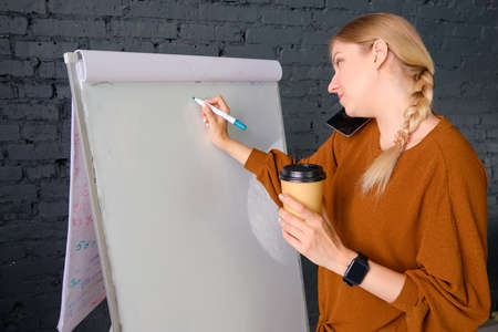 SMM manager writes on a flipchart and holds a cup of coffee.の写真素材