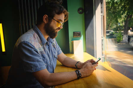 Man holds phone and chats online sitting in a cafe.
