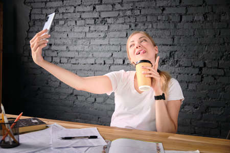 Woman taking a selfie with coffee paper cup at her workplace