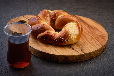 Turkish pastry acma and tea in traditional tea glass on wooden board at dark background