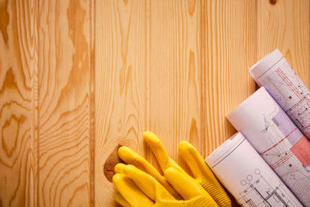 Yellow gloves and rolled drawings on wooden table