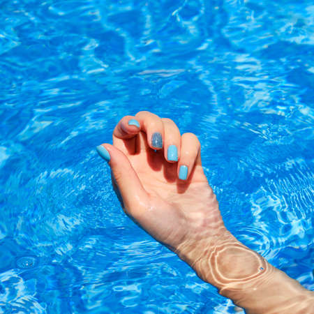 Female hands with bright manicure inside of waterの写真素材
