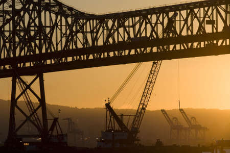 Sunrise behind the Oakland Bay Bridge and Port of Oakland cranes.の写真素材